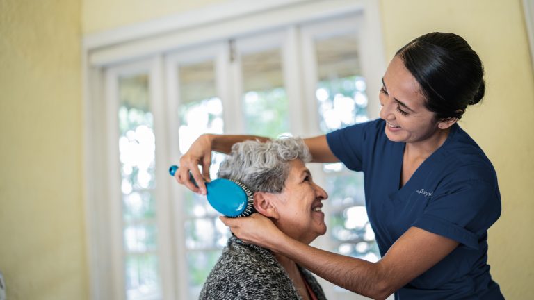 Nurse brushes an elderly woman's hair while smiling