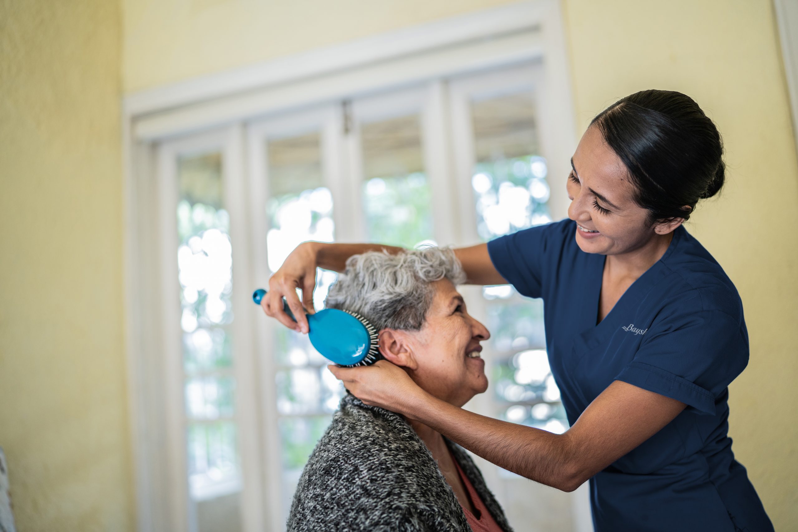 Nurse brushes an elderly woman's hair while smiling