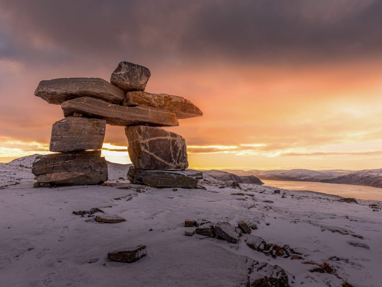 Large inukshuk on top of a snowy landscape during a sunset