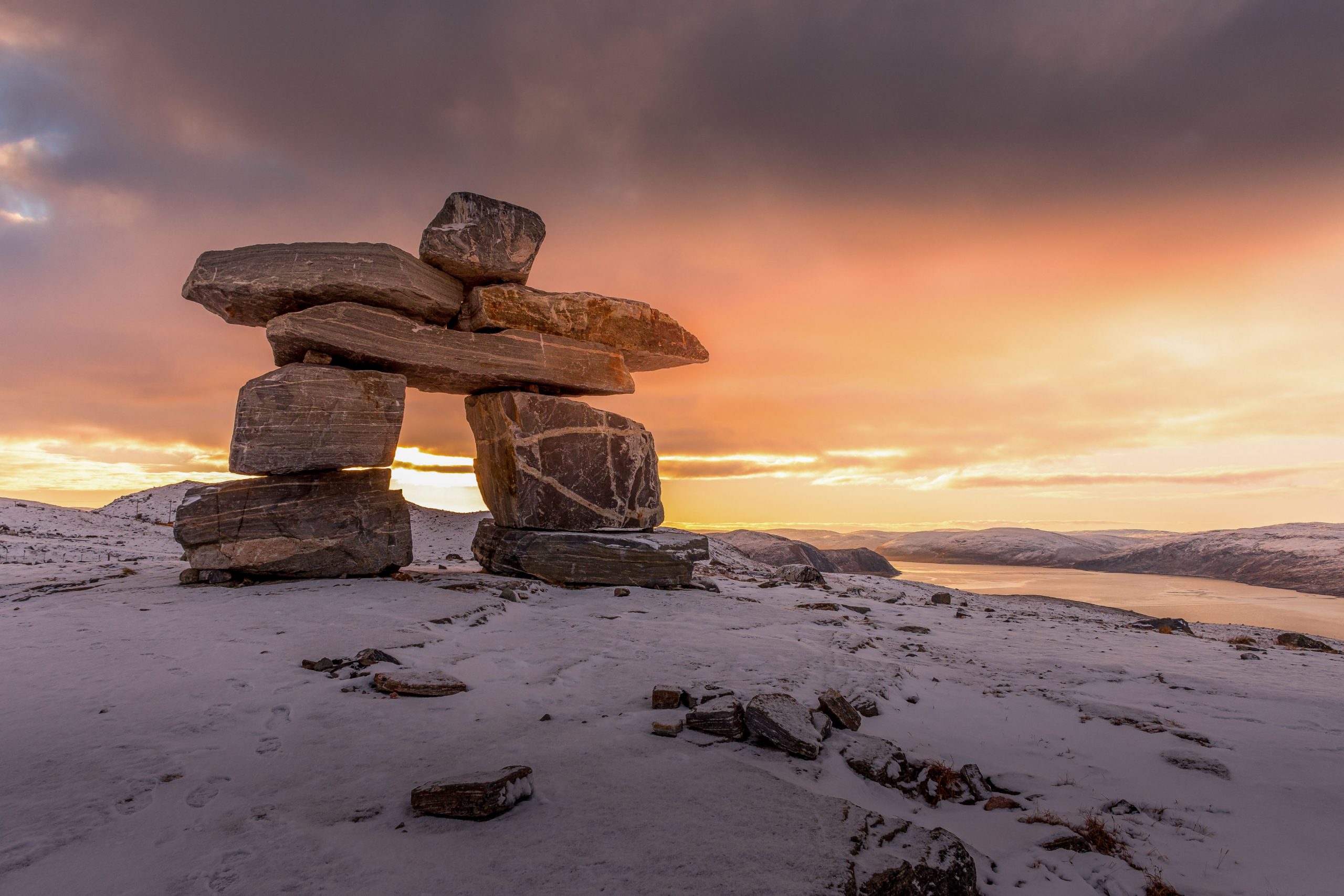 Grand inukshuk au sommet d'un paysage enneigé lors d'un coucher de soleil