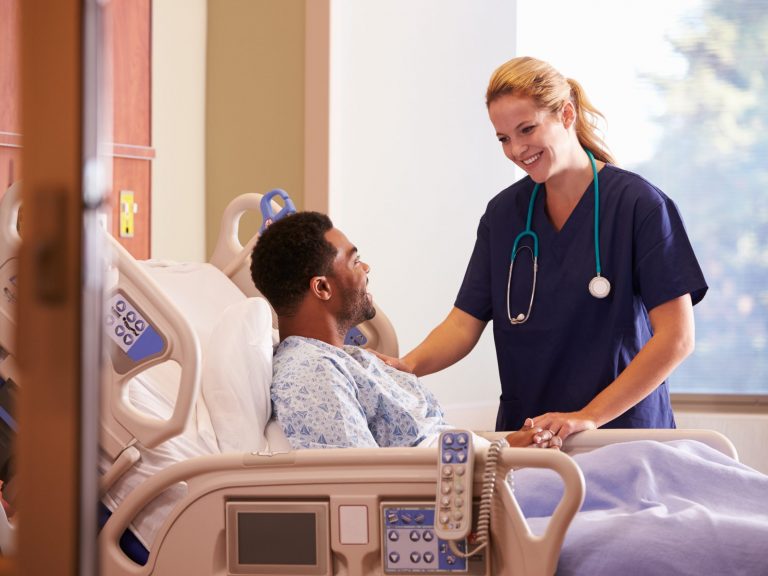 Female Doctor Talking To Male Patient In Hospital Bed