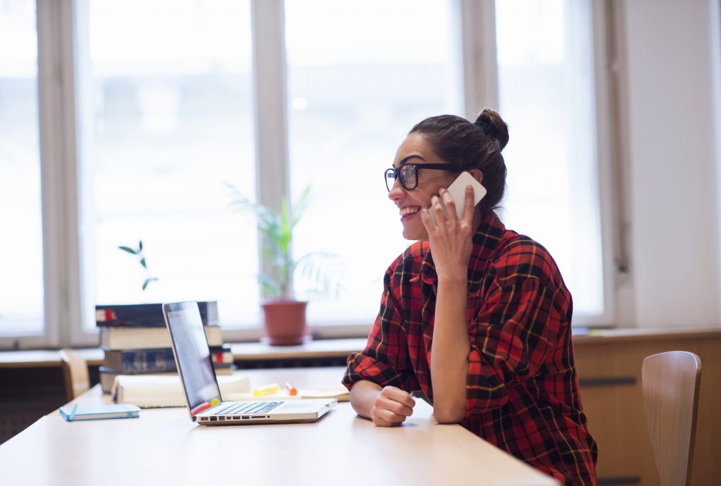 Jeune femme au téléphone devant son ordinateur portable dans un bureau