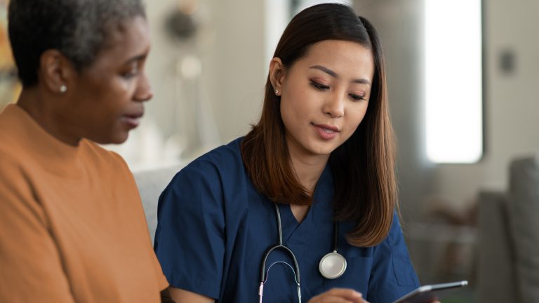 A nurse and a woman discuss something while looking at a tablet