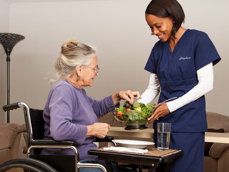 Home caregiver serving food to woman in wheelchair