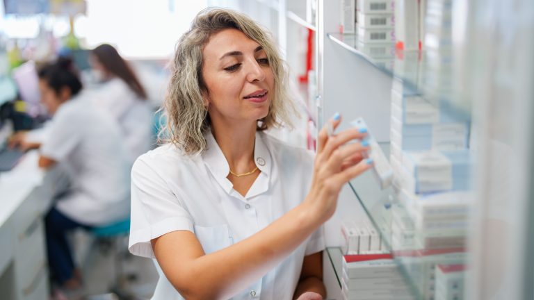 The pharmacist is taking the medicines from the shelf according to the prescription.